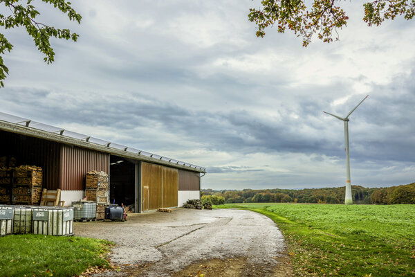 Blick von einer Scheune über ein Feld zu einem Windrad.